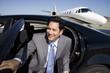 Photo: Businessman getting out of car on runway by aeroplane, smiling, portrait Businessman getting out of car on runway by aeroplane, smiling, portrait