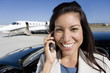 Photo: Businesswoman using mobile phone by car on runway by aeroplane, smiling, portrait, close-up Businesswoman using mobile phone by car on runway by aeroplane, smiling, portrait, close-up