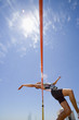 Young male athlete jumping over bar, low angle view (lens flare)