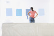 Woman holding paint roller and examining blue paint samples on living room wall