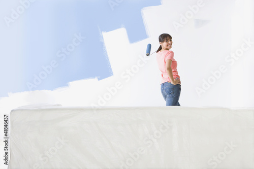 Foto: Smiling woman painting living room wall with paint roller Smiling woman painting living room wall with paint roller