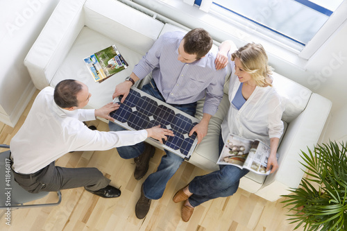 Foto: Salesman showing solar panel to couple sitting on sofa in living room Salesman showing solar panel to couple sitting on sofa in living room