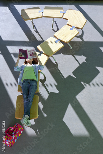Photo: Student laying on row of school desks formed into a question mark symbol studying Student laying on row of school desks formed into a question mark symbol studying
