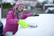 Smiling woman scraping snow from car windshield