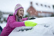 Smiling woman scraping snow from car windshield