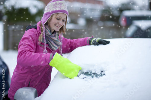 Photo: Smiling woman scraping snow from car windshield Smiling woman scraping snow from car windshield