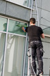gebäudereiniger steht auf der leiter und putzt fenster