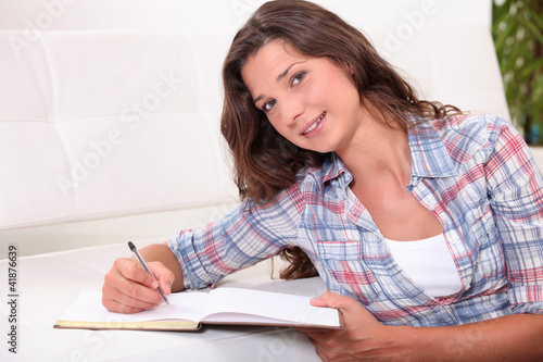 Photo: young woman writing on a notebook on a white bench young woman writing on a notebook on a white bench