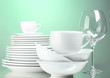 Foto: Clean plates, cups and glasses on green background Clean plates, cups and glasses on green background