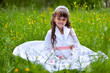 Little girl in white dress sitting in the grass and smiling