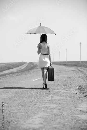 Photo: Lonely girl with suitcase and umrella at country road. Lonely girl with suitcase and umrella at country road.