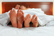 Photo: Two pairs of male and female feet seen from under the blanket Two pairs of male and female feet seen from under the blanket