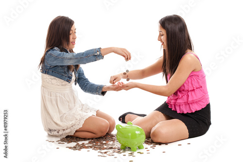 Photo: Preteen and teen sisters with piggybank isolated on white Preteen and teen sisters with piggybank isolated on white