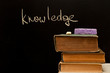 "knowledge" written on blackboard with old books