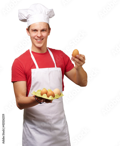 Photo: portrait of young cook man holding egg box over white background portrait of young cook man holding egg box over white background