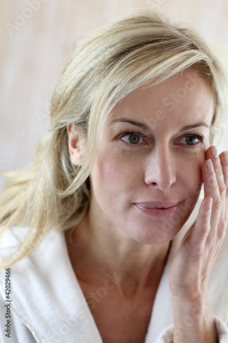 Foto: Attractive middle-aged woman applying comestics on her face Attractive middle-aged woman applying comestics on her face