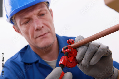 Photo: plumber cutting a copper pipe with a pipe cutter plumber cutting a copper pipe with a pipe cutter