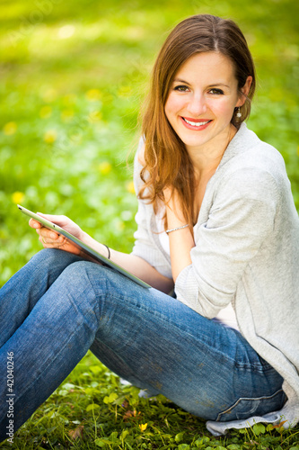 Foto: Young woman using her tablet computer while relaxing outdoors Young woman using her tablet computer while relaxing outdoors