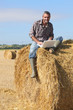 Farmer with a laptop sitting on a haystack