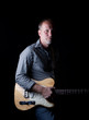 Shadow filled shot of a rugged looking guitar player