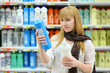 Photo: Beautiful girl wearing scarf compares abstergents in shop Beautiful girl wearing scarf compares abstergents in shop