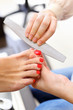 Female hands make pedicure by nail files for client in salon