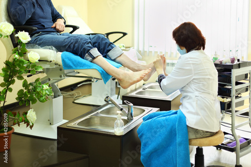 Photo: Woman wearing coat does foot massage for man in beauty salon Woman wearing coat does foot massage for man in beauty salon