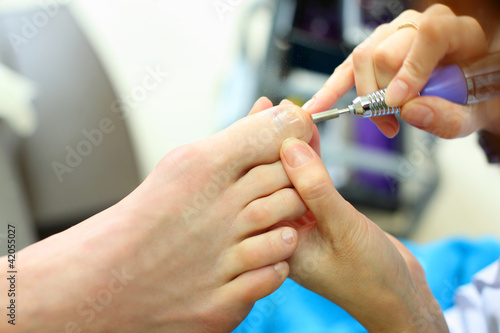 Photo: Female hands polish male toes by special machine in beauty salon Female hands polish male toes by special machine in beauty salon