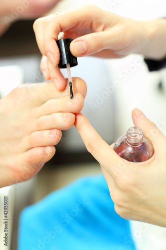 Photo: Female hands cover male toenails by transparent nail polish Female hands cover male toenails by transparent nail polish