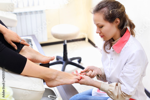 Photo: Woman wearing white coat makes pedicure for client in salon Woman wearing white coat makes pedicure for client in salon