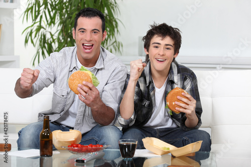 Foto: Father and son eating burgers in front of TV Father and son eating burgers in front of TV