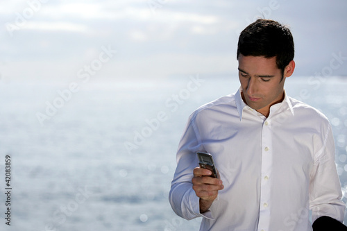 Foto: Man sending an SMS by the water's edge Man sending an SMS by the water's edge