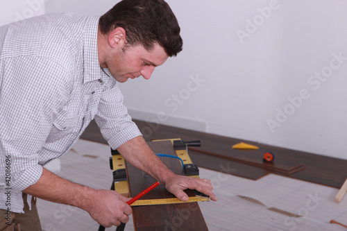 Photo: Man laying a floor and measuring a piece of wood Man laying a floor and measuring a piece of wood