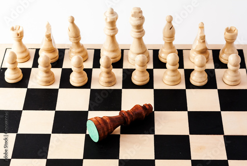 Photo: Shot of an chess board with a fallen king in front many pieces Shot of an chess board with a fallen king in front many pieces