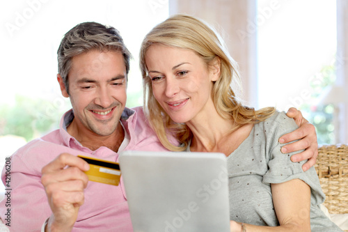 Photo: Couple sitting in sofa at home and doing online shopping Couple sitting in sofa at home and doing online shopping