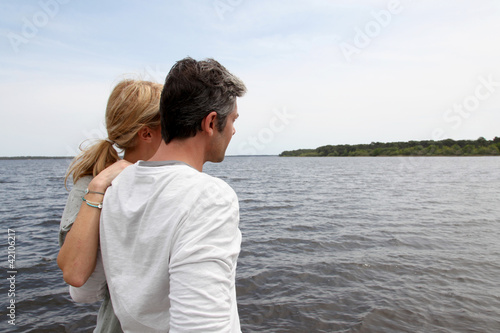 Photo: Profile view of couple sitting on a wooden bridge by a lake Profile view of couple sitting on a wooden bridge by a lake