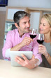 Couple in kitchen with glass of wine websurfing on tablet