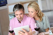Couple in kitchen with glass of wine websurfing on tablet