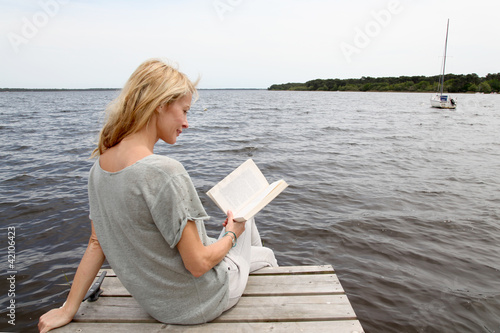 Foto: Woman reading book sitting on lake boardwalk Woman reading book sitting on lake boardwalk