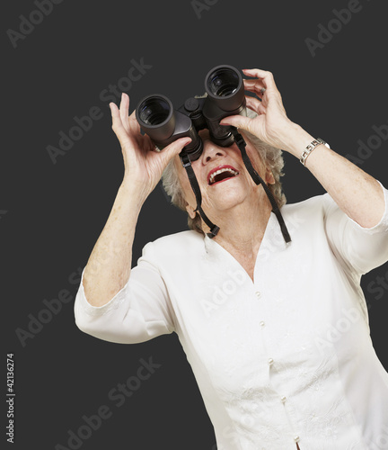 Photo: portrait of senior woman looking through a binoculars against a portrait of senior woman looking through a binoculars against a