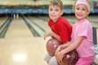 Happy brother and sister sit and hold balls in bowling club