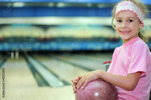Photo: Little girl sits and holds ball in bowling club Little girl sits and holds ball in bowling club