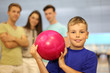 Smiling boy dressed in T-shirt holds pink ball in bowling club