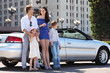 Happy father, mother and two children stand near convertible car