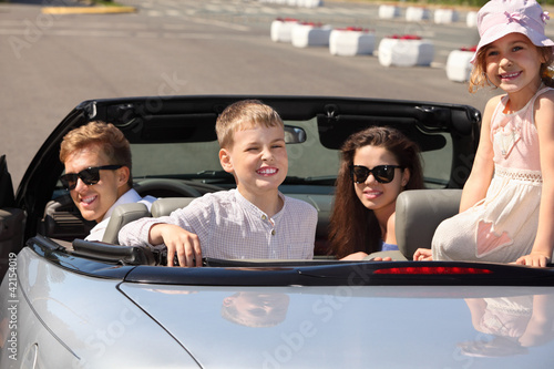 Photo: Happy father, mother and two children sit in convertible car Happy father, mother and two children sit in convertible car