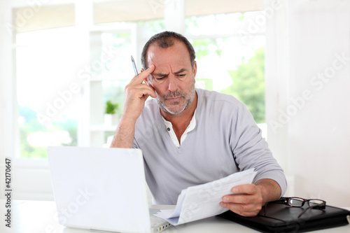 Photo: Senior man being puzzled with tax documents Senior man being puzzled with tax documents