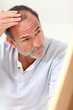 Senior man looking at his hair in mirror