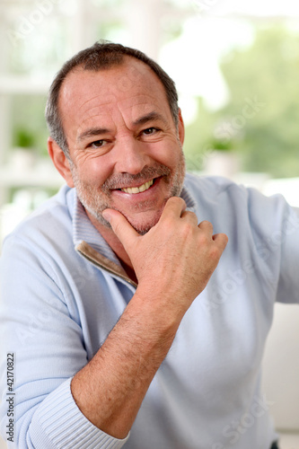 Photo: Portrait of senior man sitting in sofa at home Portrait of senior man sitting in sofa at home