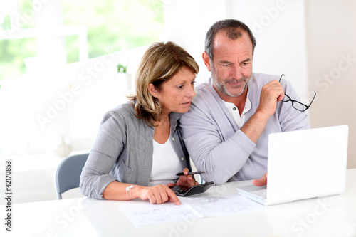 Photo: Couple reading construction plan at home with use of laptop Couple reading construction plan at home with use of laptop