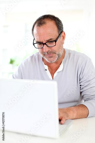 Photo: Senior businessman working on laptop from home Senior businessman working on laptop from home